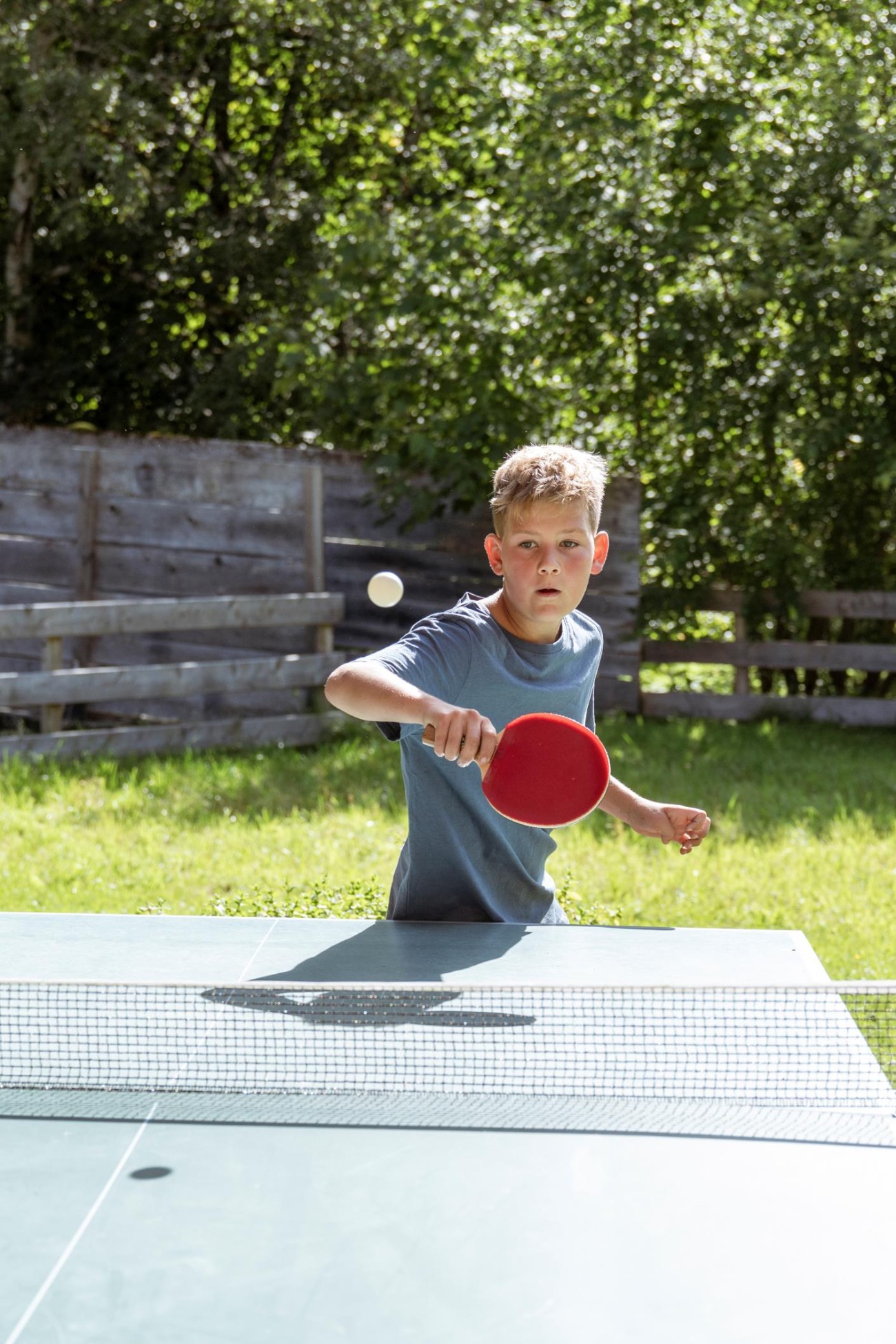 Ein Junge spielt Tischtennis im Freien an einem sonnigen Tag