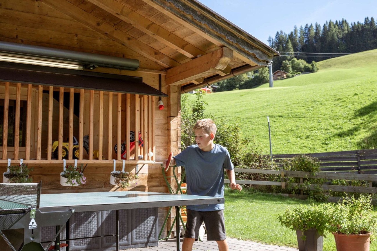 Ein Junge spielt Tischtennis vor einem Holzhaus im Hotel Bachschmied