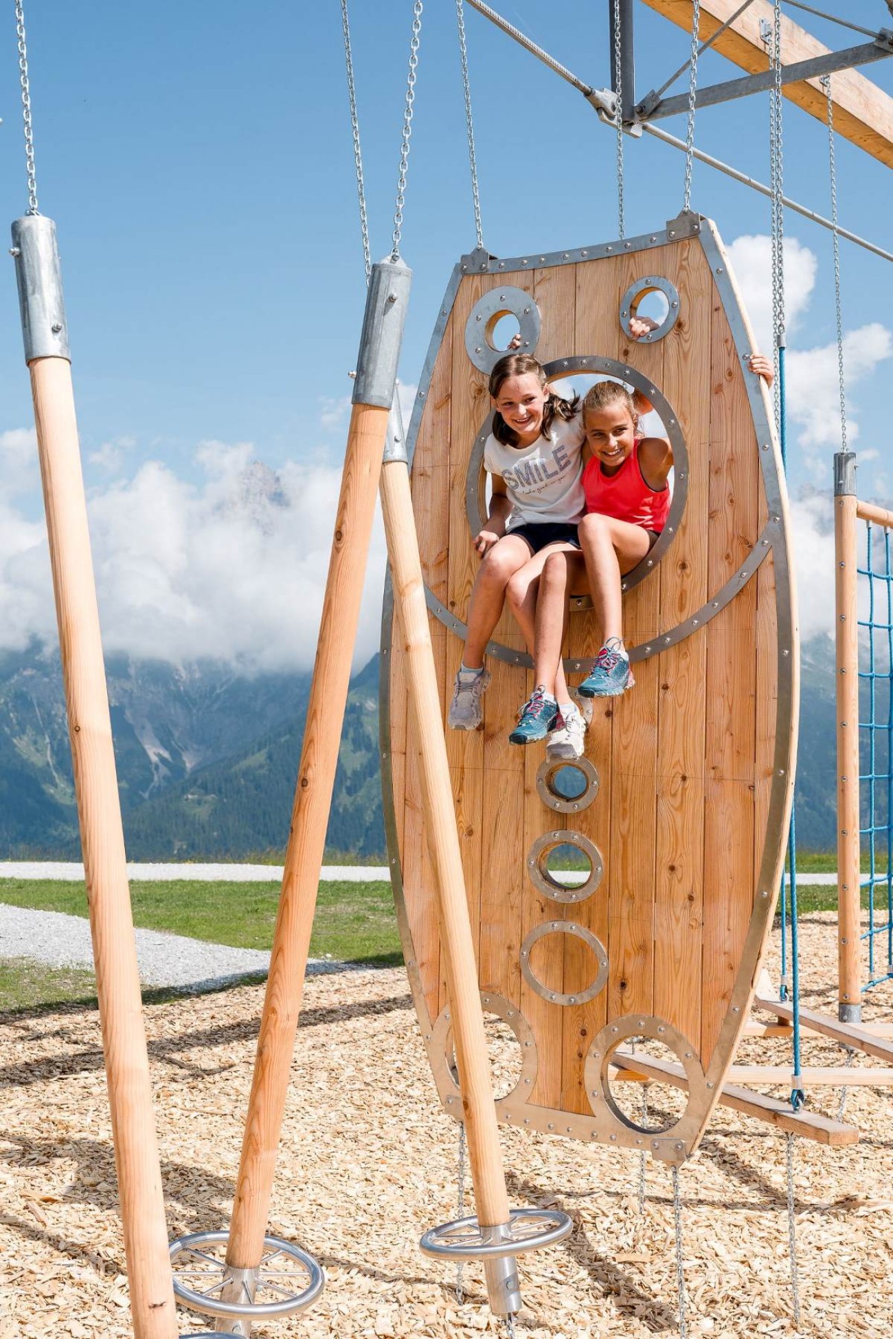 Zwei Kinder klettern auf einem h&ouml;lzernen Kletterger&uuml;st im Freien mit Bergkulisse. &copy;TVB_Hochk&ouml;nig
