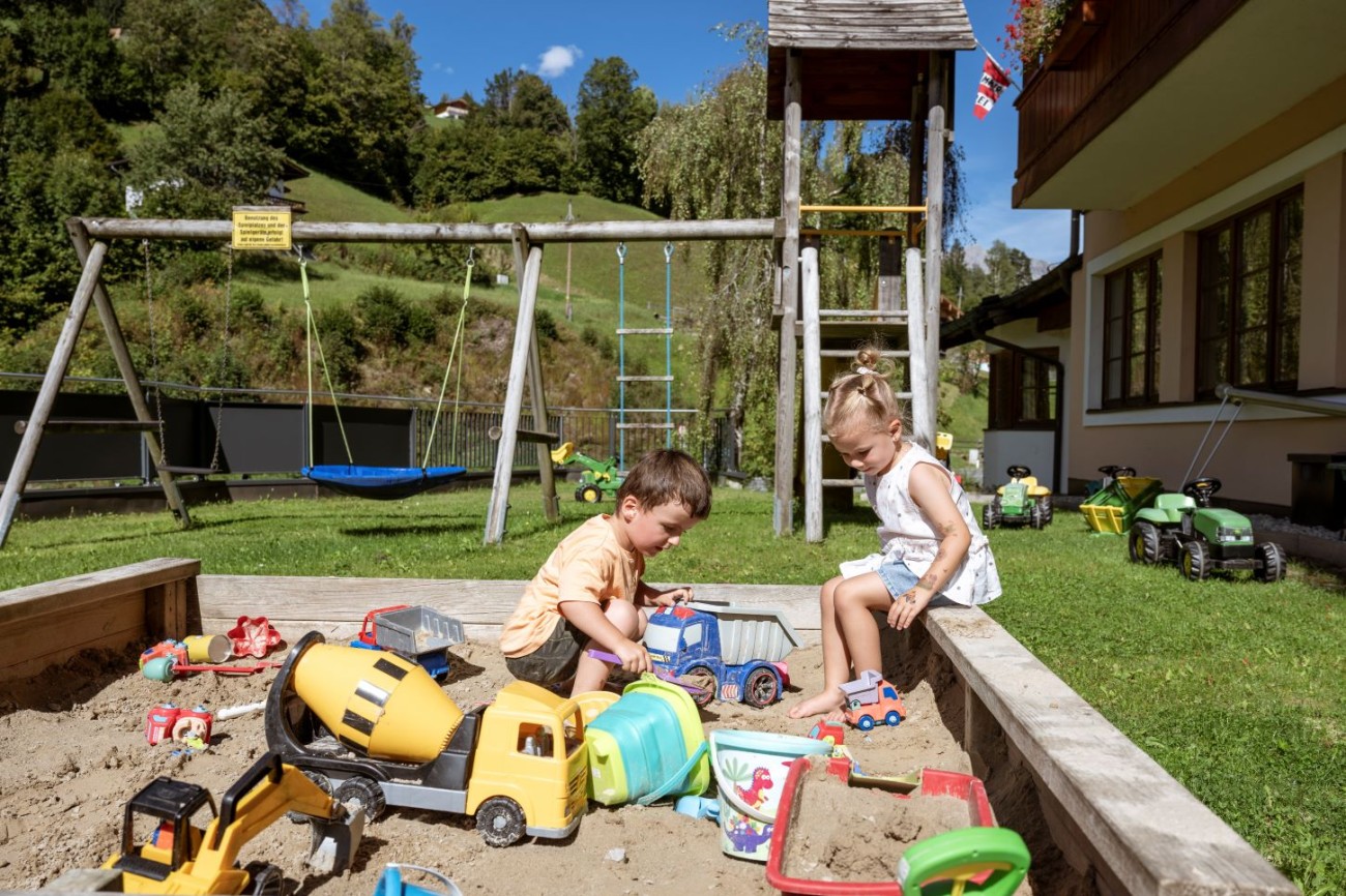 Zwei Kinder spielen mit Spielzeugautos im Sandkasten am Spielplatz des Hotel Bachschmied