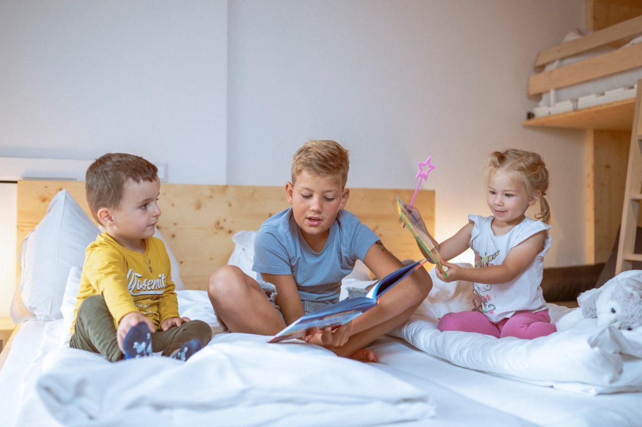 Drei junge Kinder sitzen im Bett im Hotel Bachschmied und lesen B&uuml;cher. 