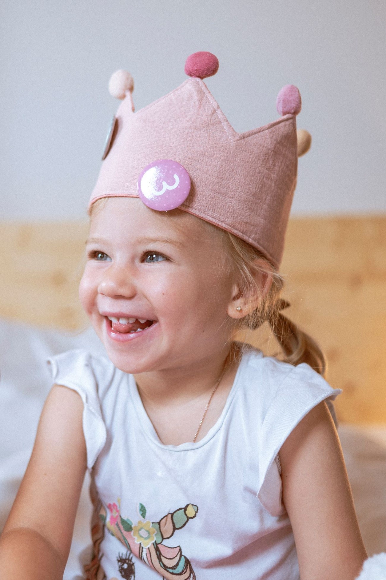 M&auml;dchen mit Z&ouml;pfen und rosa Krone lacht im Hotelzimmer vom Hotel Bachschmied in Maria Alm.