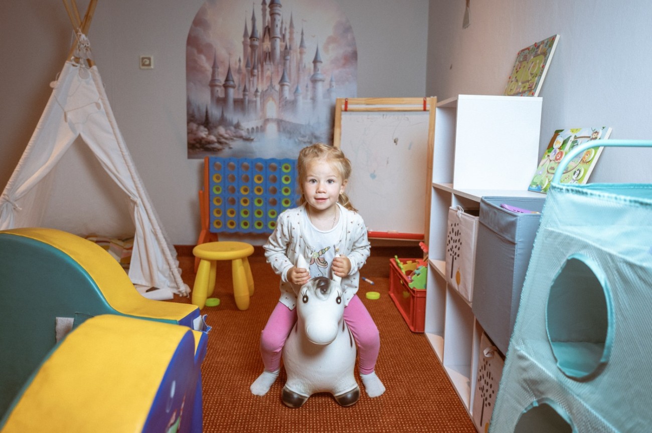 Blondes M&auml;dchen sitzt auf Spielpferd im Spielzimmer vom Hotel Bachschmied im Salzburger Land.