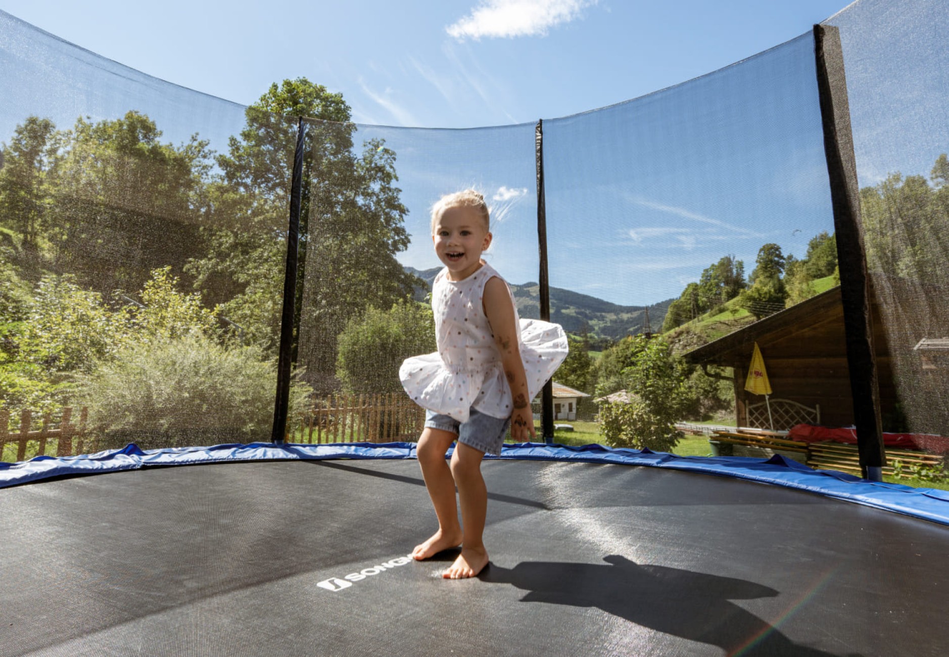 Junges M&auml;dchen h&uuml;pft im Trampolin vom Hotel Bachschmied und lacht.