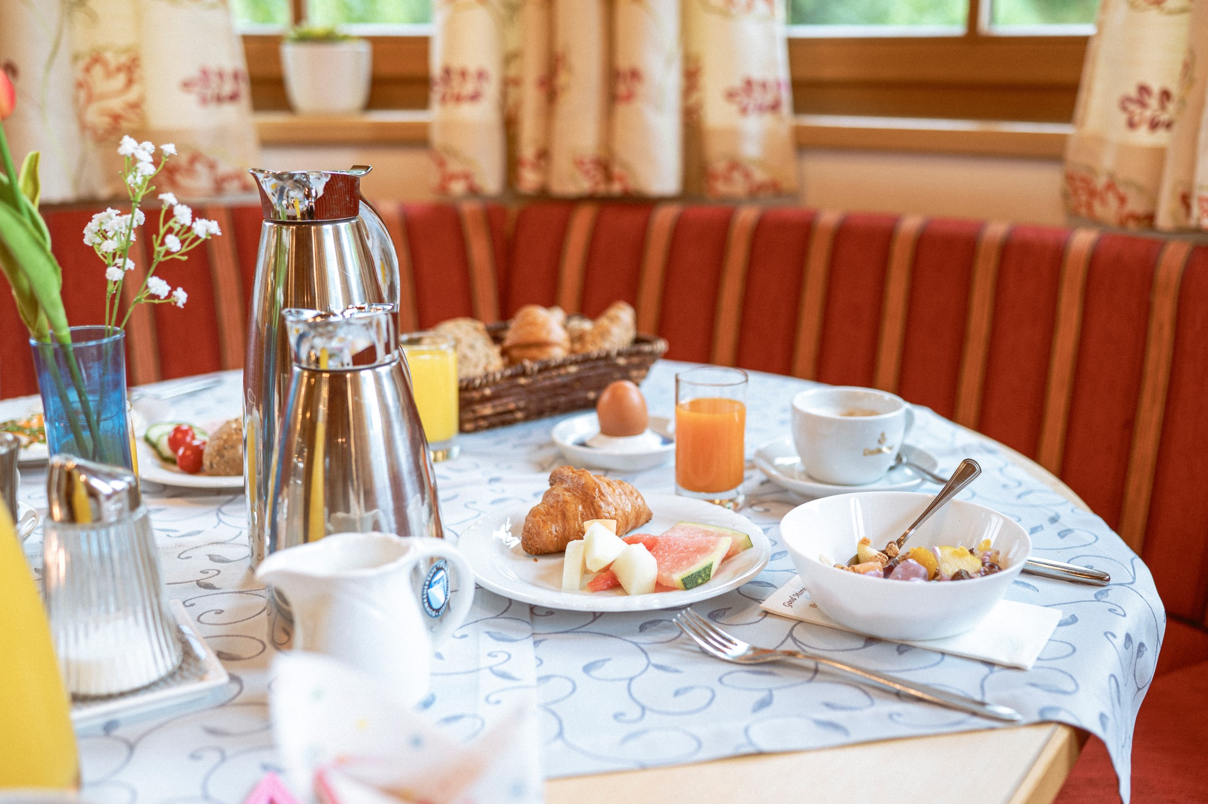 Frühstückstisch mit Obst, Croissant, Saft und Kaffee auf einem gedeckten Tisch.