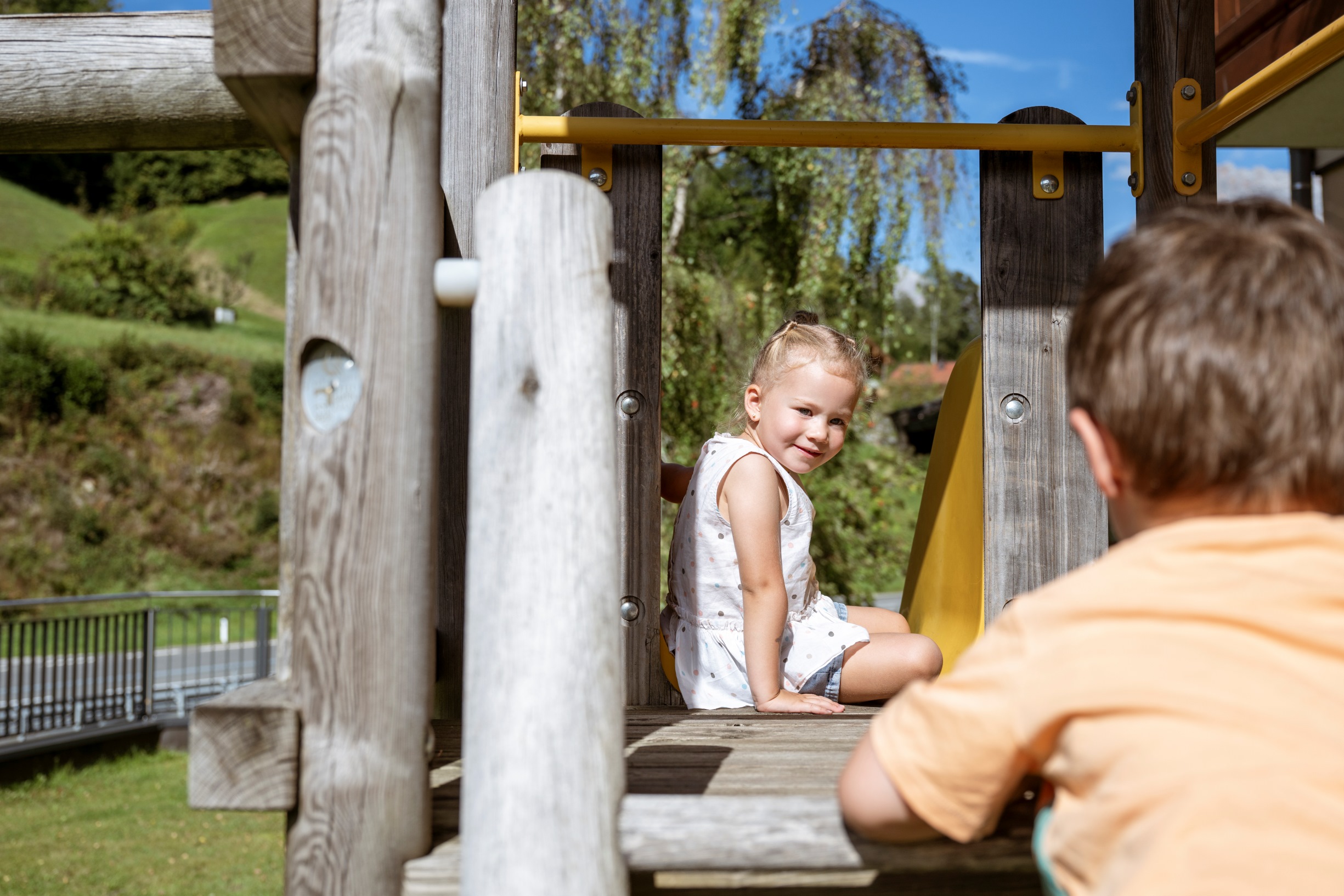 Ein junges Mädchen sitzt lachend auf einer Rutsche auf dem Spielplatz des Hotel Bachschmied.