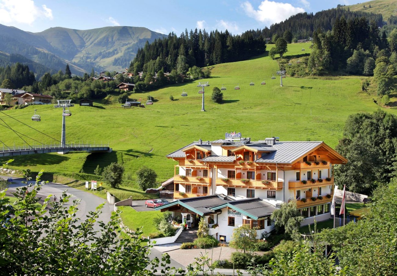 Hotel Bachschmied in den Bergen, umgeben von gr&uuml;nen H&uuml;geln und Seilbahnen im Sonnenschein