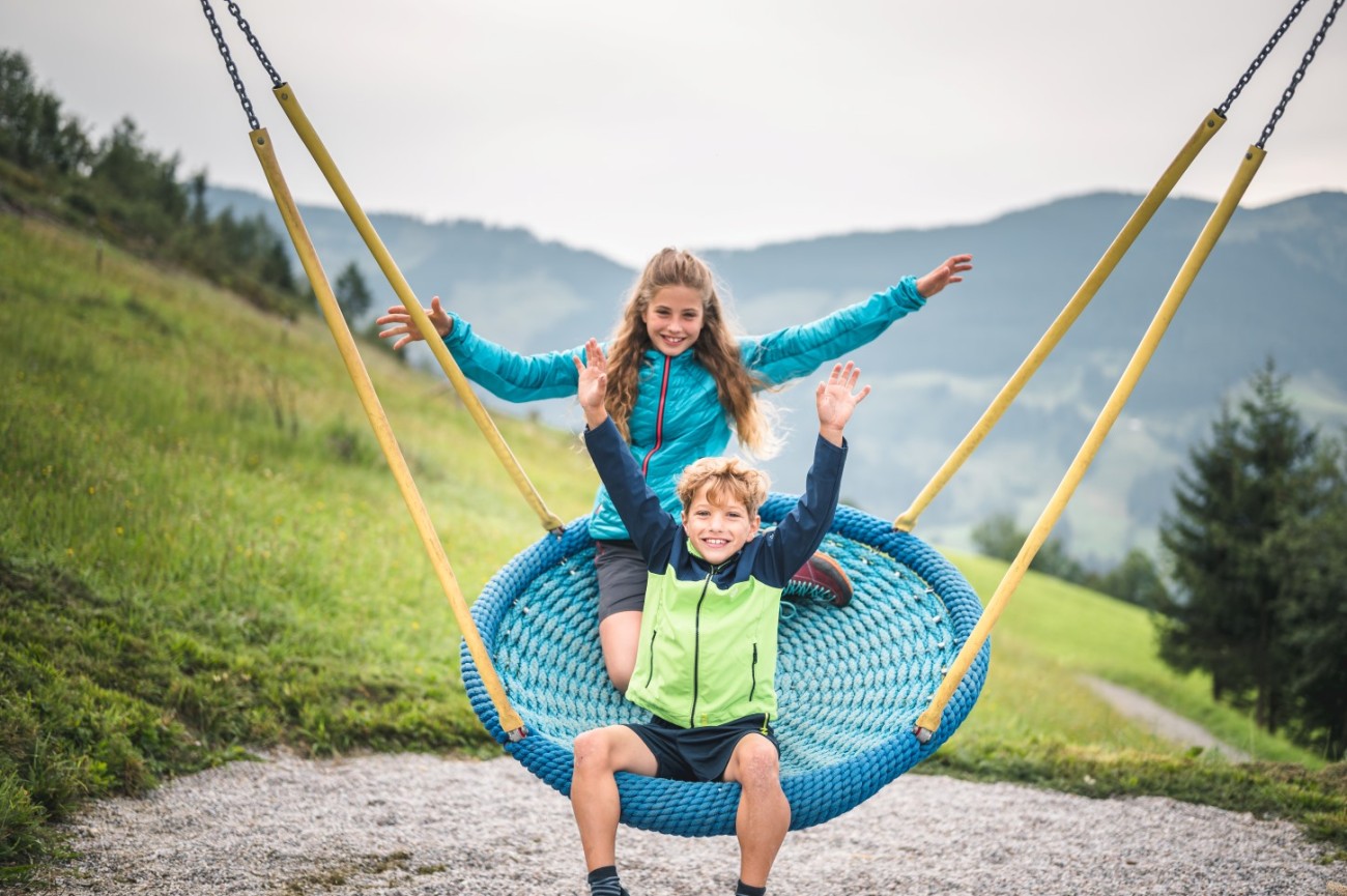 Zwei Kinder schaukeln fr&ouml;hlich auf einer gro&szlig;en blauen Schaukel im Gr&uuml;nen am Hochk&ouml;nig. &copy;TVB_Hochk&ouml;nig
