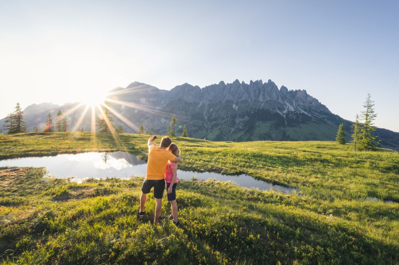 Ein Paar umarmt sich in einer Berglandschaft mit Sonnenschein und Spiegelung im Wasser im Urlaub in Maria Alm. &copy;TVB_Hochk&ouml;nig
