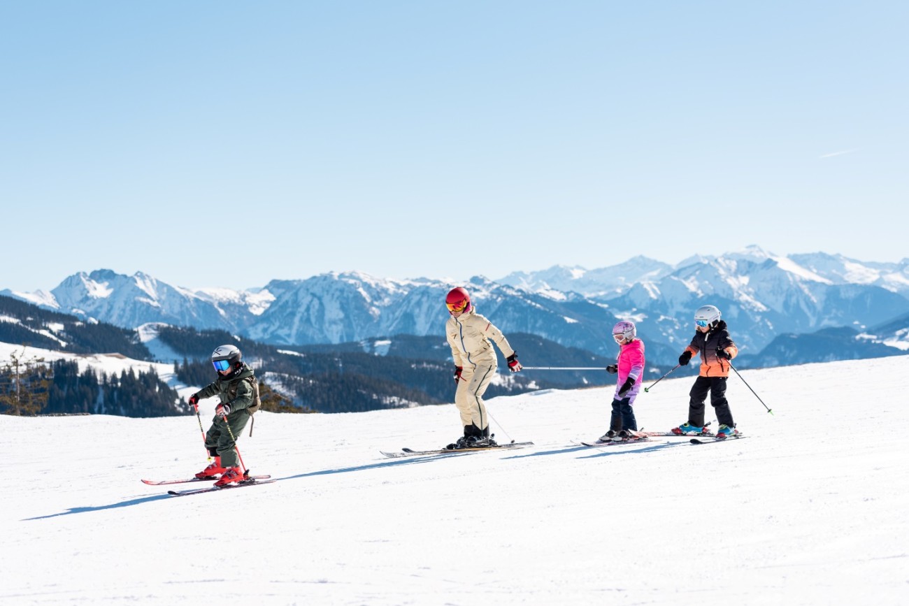 Eine Person und drei Kinder fahren bei sonnigem Wetter Ski in den Bergen von Hochk&ouml;nig. &copy;TVB Hochk&ouml;nig/Miriam Lottes
