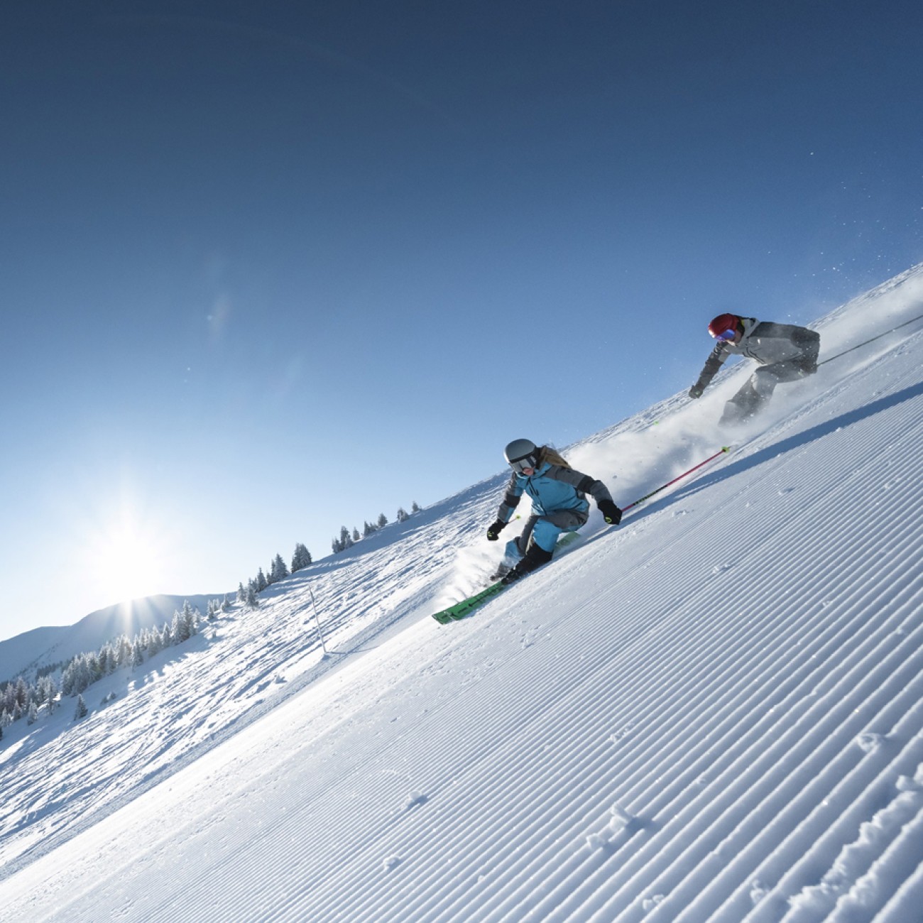 Zwei Skifahrer fahren eine sonnige Piste mit frisch pr&auml;pariertem Schnee hinunter. &copy;TVB Hochk&ouml;nig