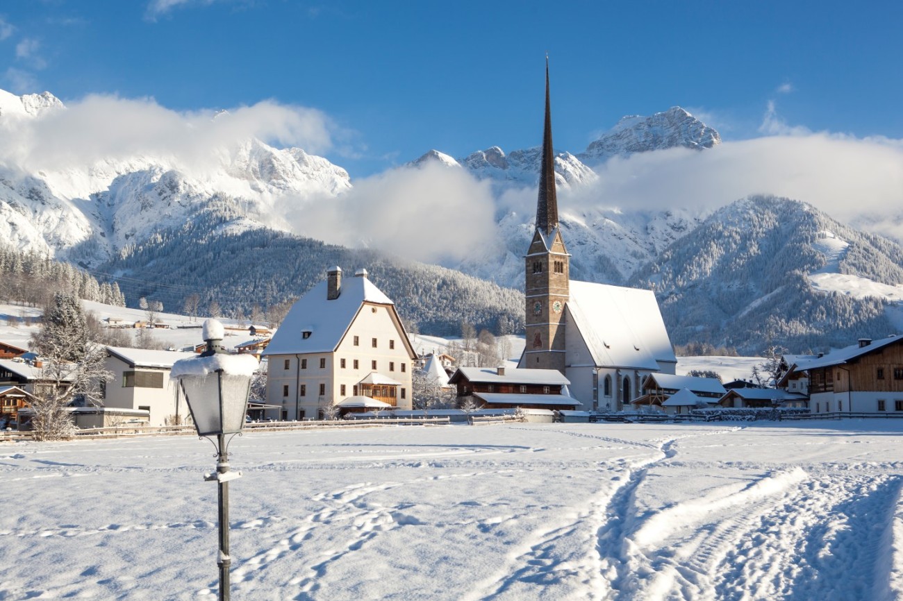 Verschneite Landschaft mit Kirche und Bergen im Hintergrund an einem klaren, sonnigen Tag im Winterurlaub am Hochk&ouml;nig. &copy;TVB_Hochk&ouml;nig