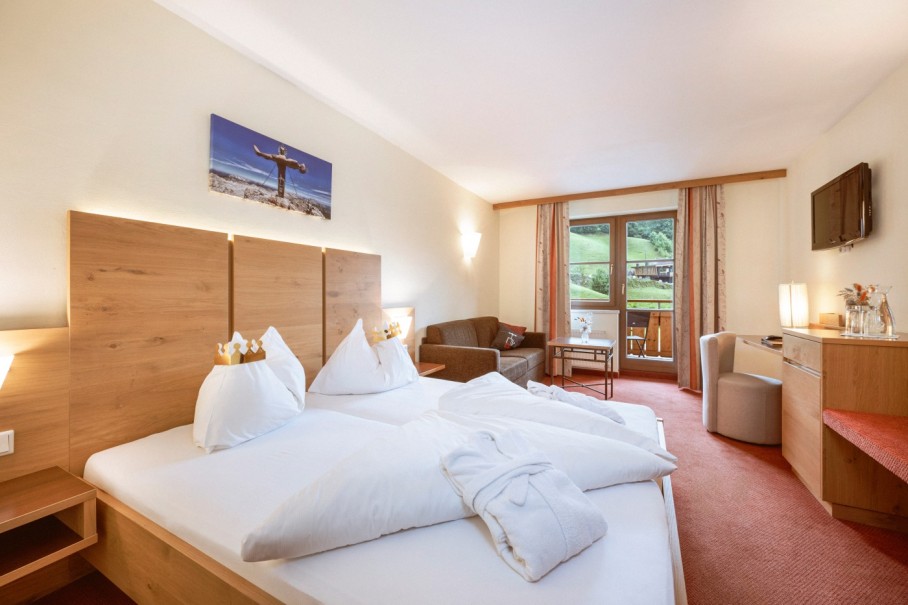 Helles Hotelzimmer mit Doppelbett, Sofa und Balkon im Bachschmied in Maria Alm.