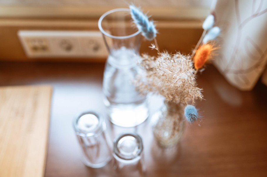 Wasserkaraffe und Tischdeko mit bunten Gr&auml;sern im Doppelzimmer im Hotel Bachschmied.