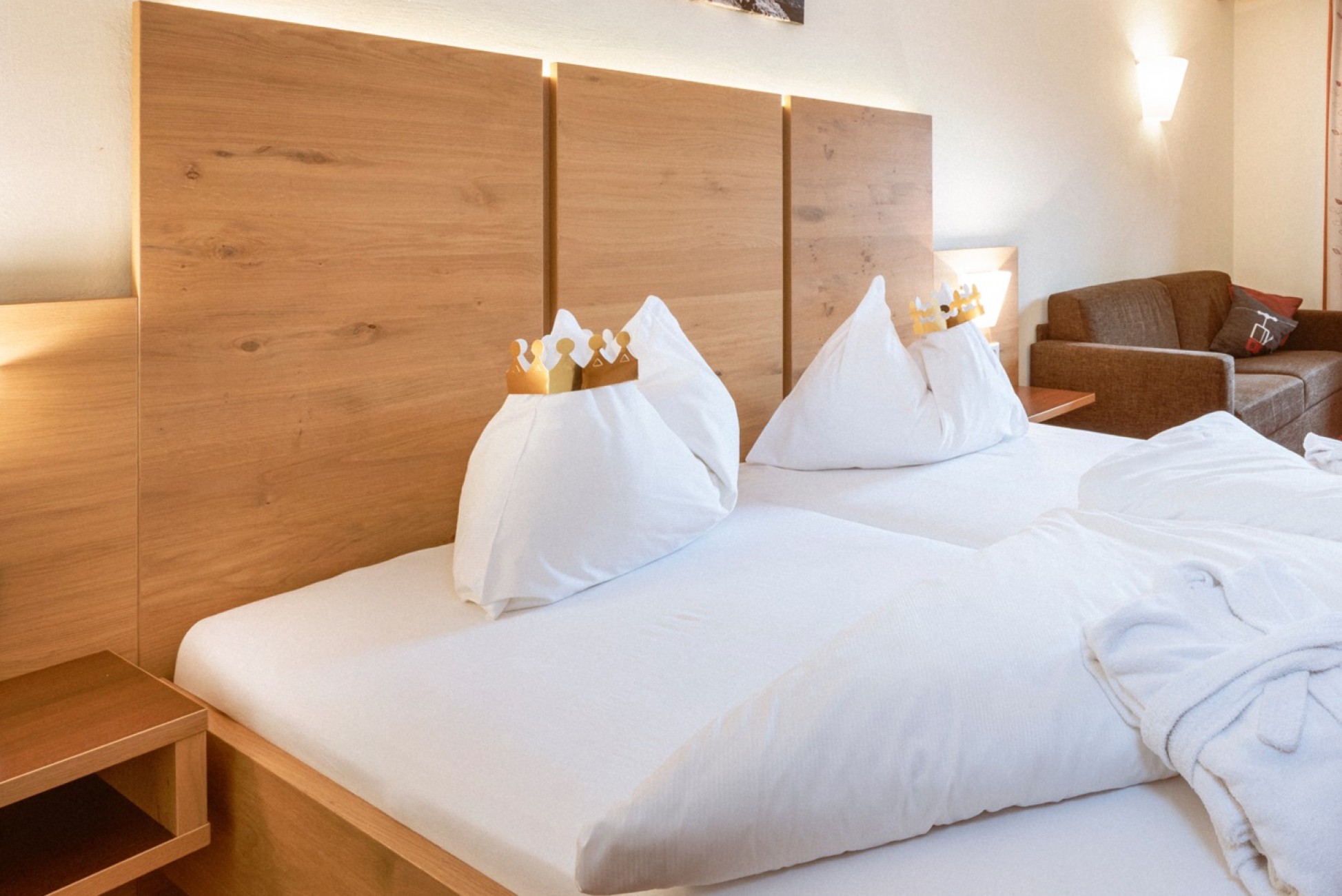 Ein Doppelbett im Hotel Bachschmied mit Holzkopfteilen, auf den Kissen liegen Papierkronen.