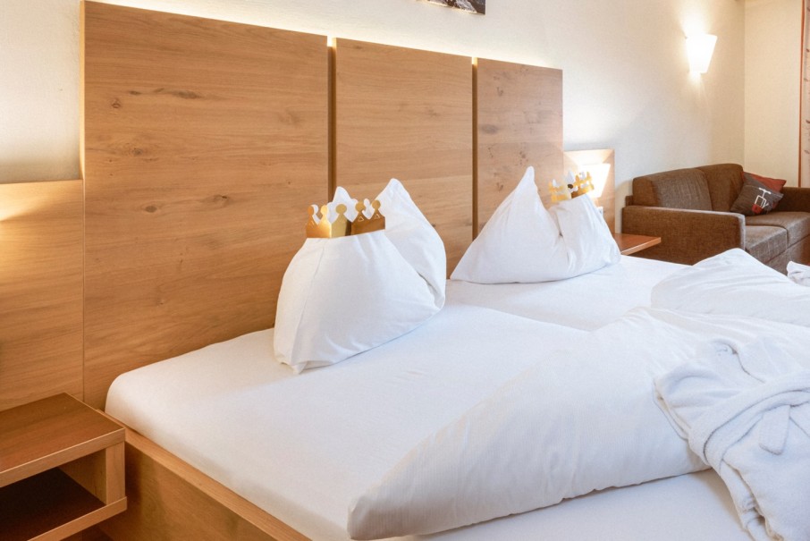 Ein Doppelbett im Hotel Bachschmied mit Holzkopfteilen, auf den Kissen liegen Papierkronen.