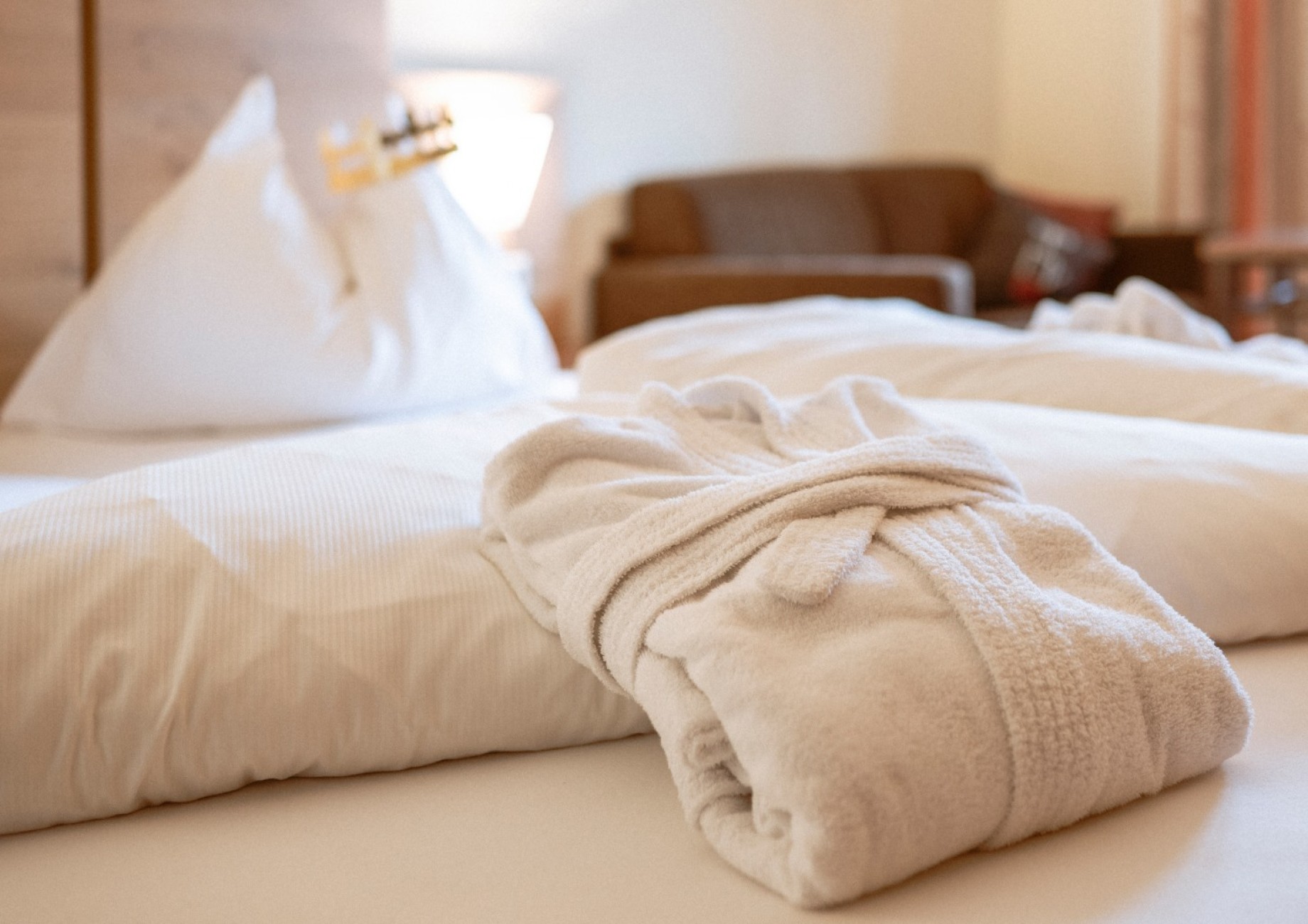 Ein wei&szlig;er Bademantel liegt auf einem gemachten Bett in einem gem&uuml;tlichen Zimmer des Hotel Bachschmied.