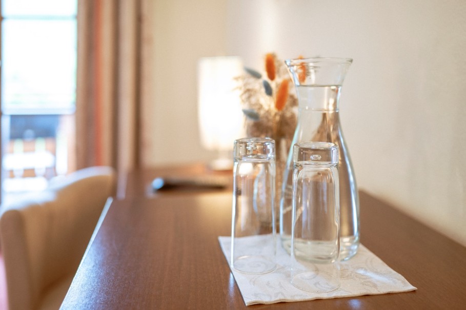 Eine Glaskaraffe und zwei Gl&auml;ser stehen auf einem Tischl&auml;ufer auf einem Holztisch.