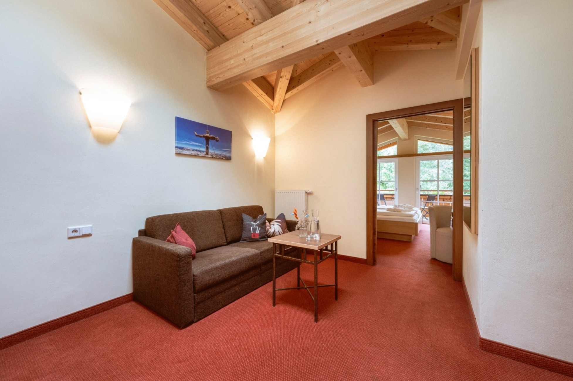 Wohnzimmer mit brauner ausziehbarer Couch, kleinem Tisch und Blick ins Schlafzimmer im Familienzimmer Deluxe.