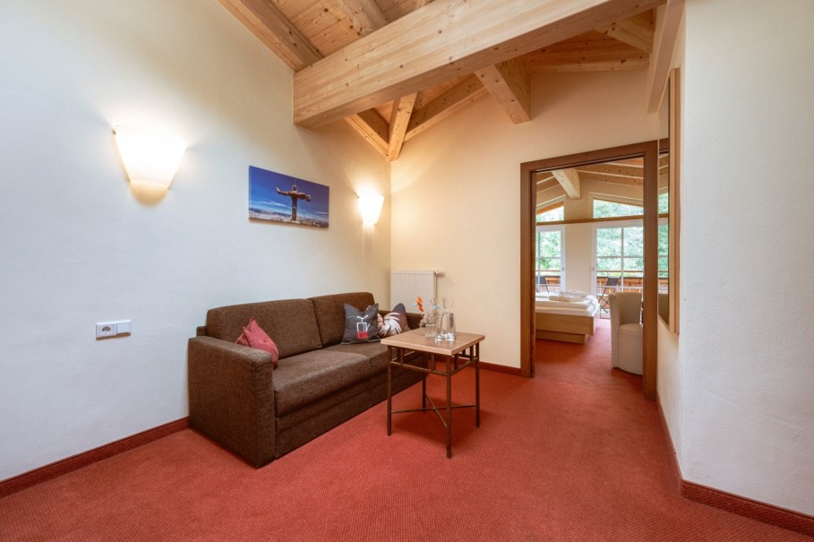 Wohnzimmer mit brauner ausziehbarer Couch, kleinem Tisch und Blick ins Schlafzimmer im Familienzimmer Deluxe.