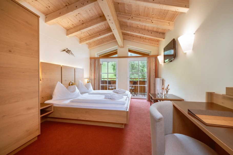 Helles Hotelzimmer mit Holzm&ouml;beln und Balkonblick auf die Natur im Familienzimmer Deluxe im Hotel Bachschmied.