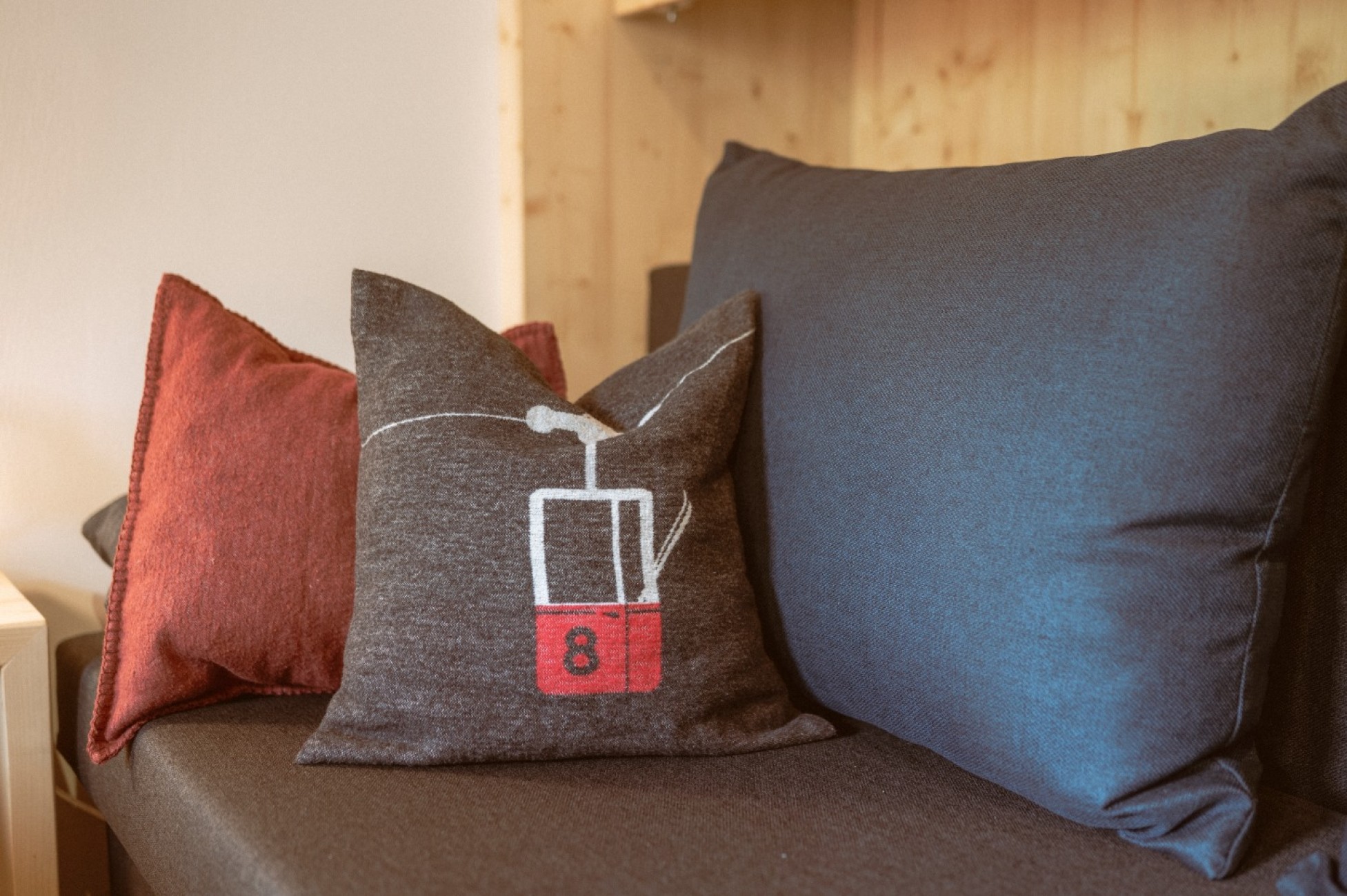 Drei Kissen auf einem Sofa, eines mit einem Seilbahn-Motiv im Dopplezimmer im Hotel Bachschmied.